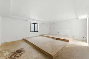 Spacious unfinished room featuring a recessed ceiling, a dark-framed window, and a multi-level platform structure