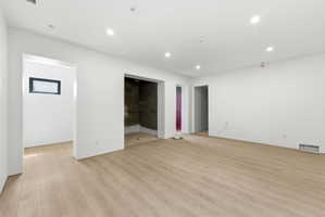 Spacious room featuring light wood-finish flooring, recessed lighting, and crisp white walls