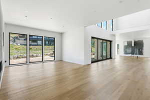 Spacious interior featuring light wood-finish flooring, white walls, and multiple large windows with black frames