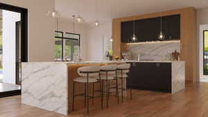 Modern kitchen featuring a waterfall island with integrated lighting, wood-finish flooring, black cabinetry, a full-height stone backsplash, and pendant lighting fixtures