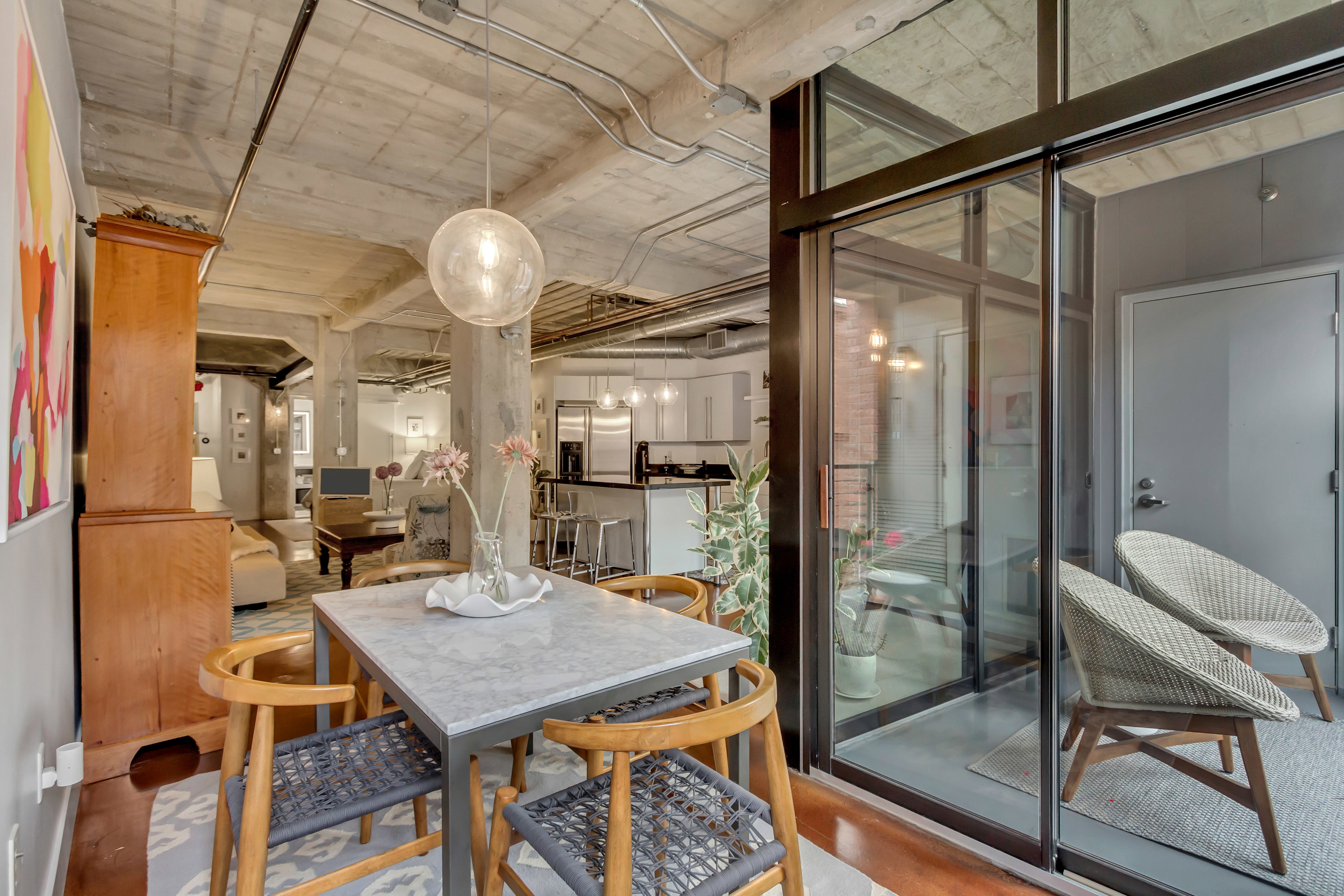 Open-concept living area featuring a concrete ceiling with exposed conduit, a dining area with a stone-finish table, and a glass-enclosed patio