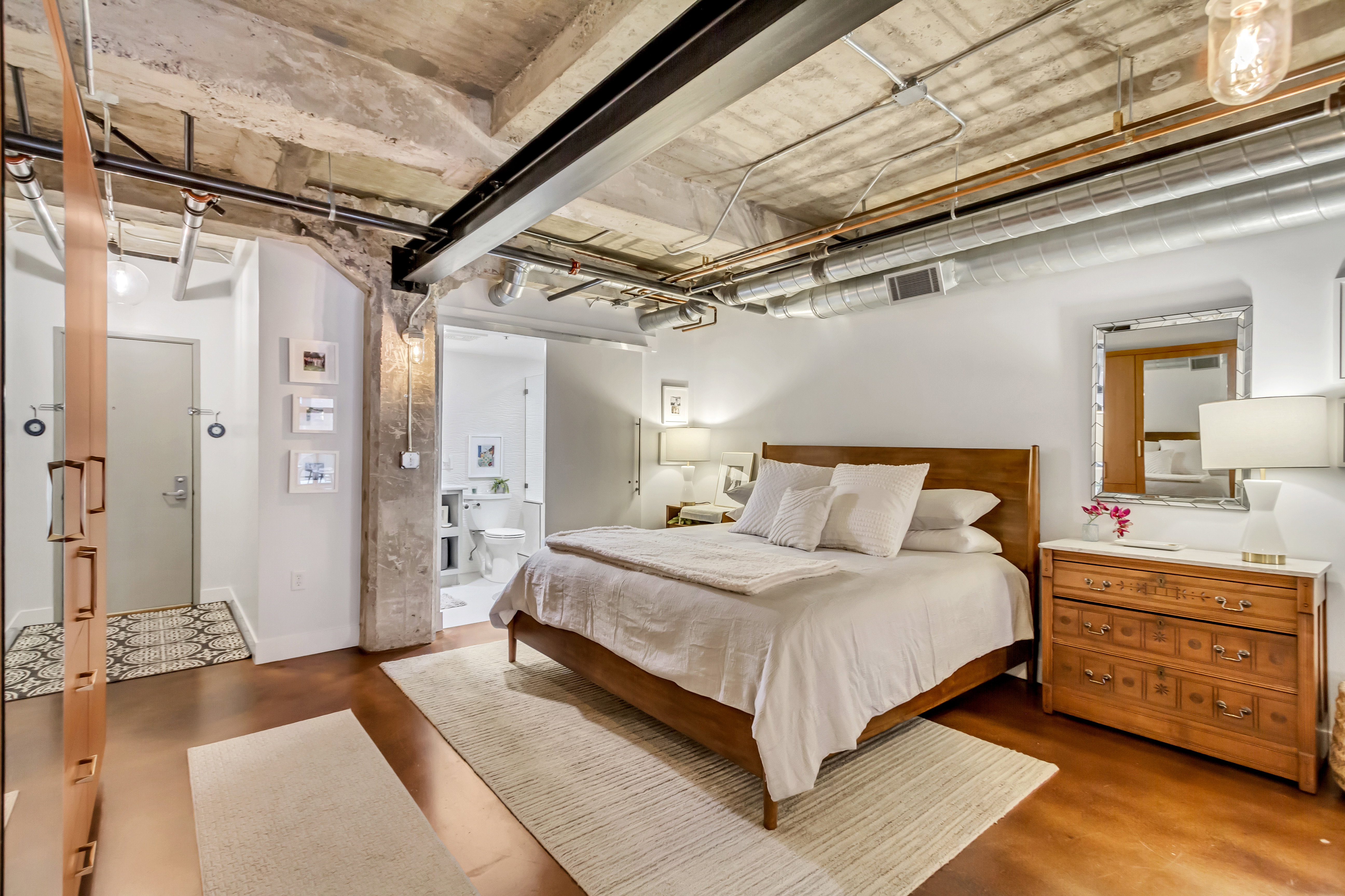 Exposed concrete ceilings with industrial-style ductwork and conduits, wood-finish flooring, and white wall finishes