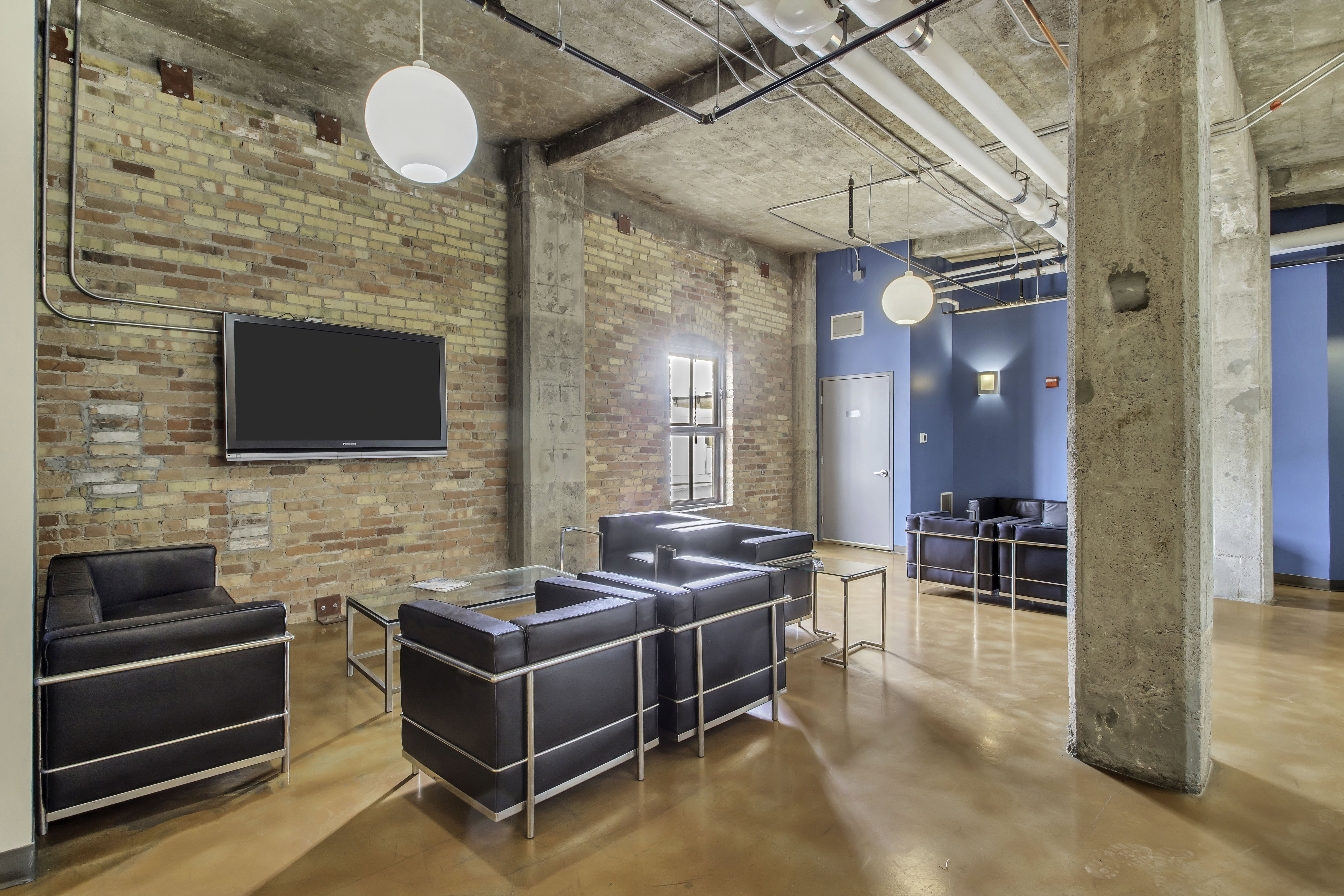 Exposed brick wall with mounted television, concrete ceiling, and industrial-style pendant lighting