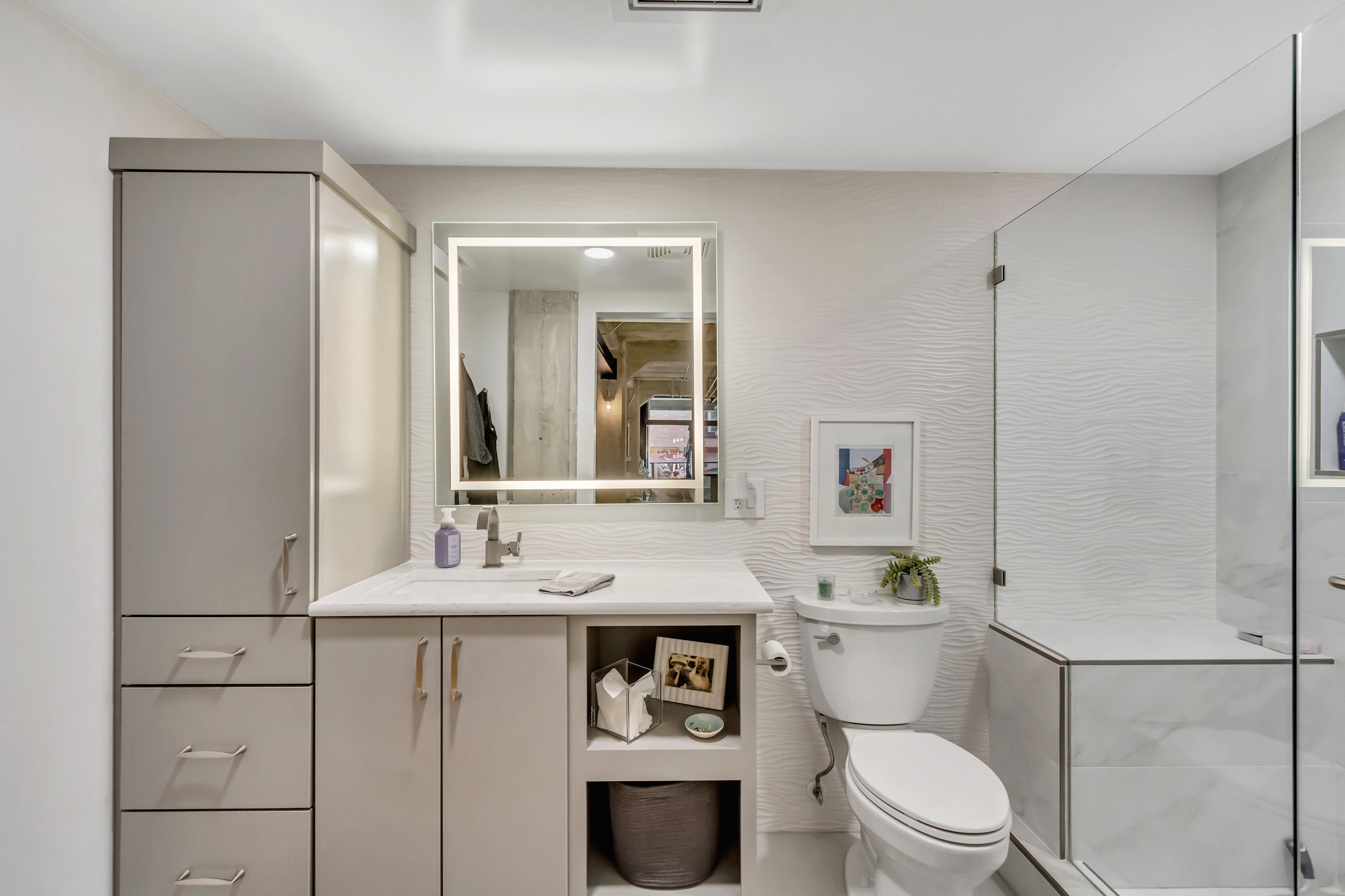 Bathroom featuring a frameless glass shower enclosure, a vanity with integrated sink, and an illuminated mirror