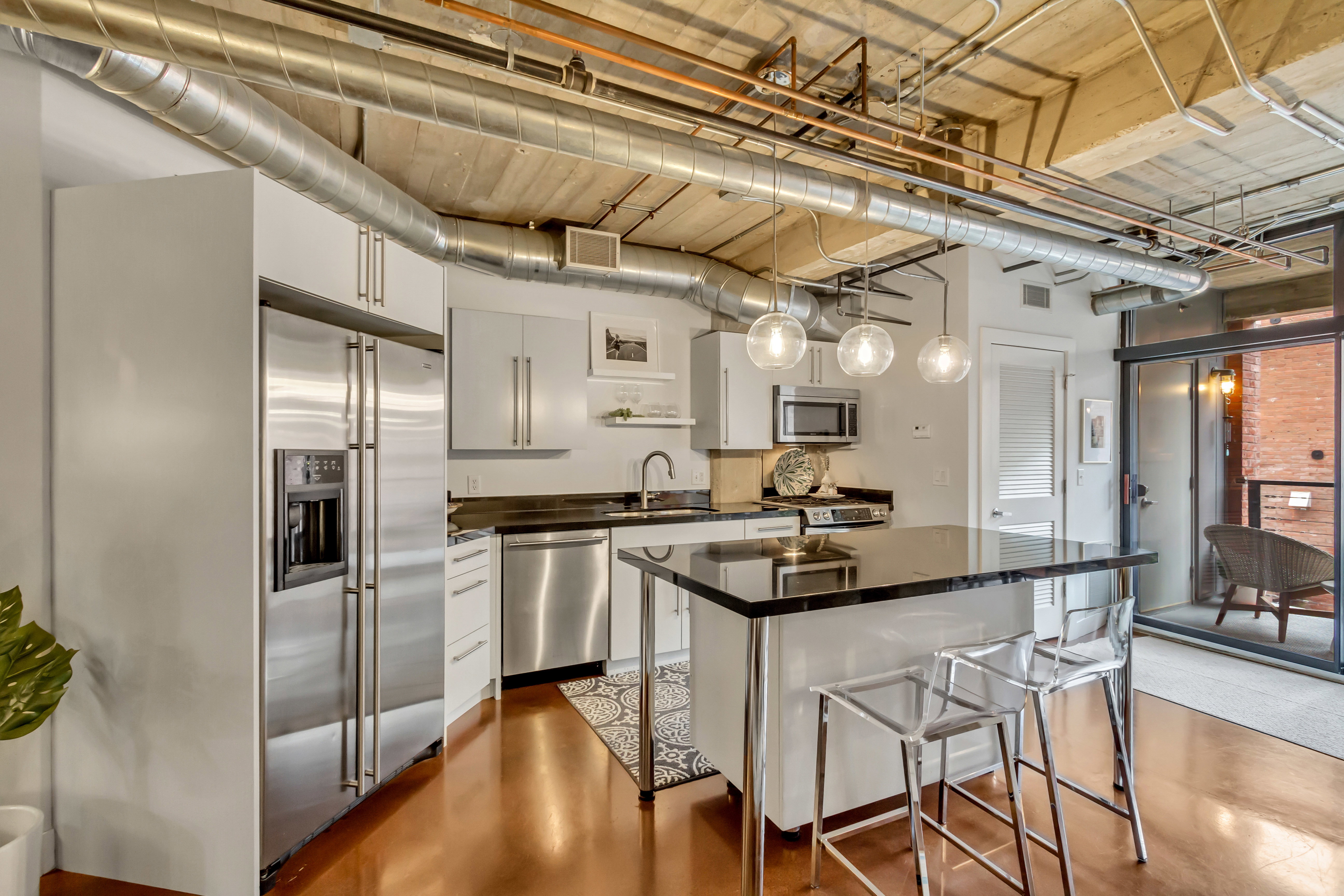 Open-concept kitchen featuring stainless steel appliances, white cabinetry, dark countertops, and a central island with pendant lighting