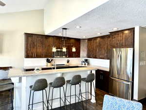Kitchen featuring dark wood cabinetry, light-toned countertops, a white subway tile backsplash, recessed lighting, and a stainless steel refrigerator