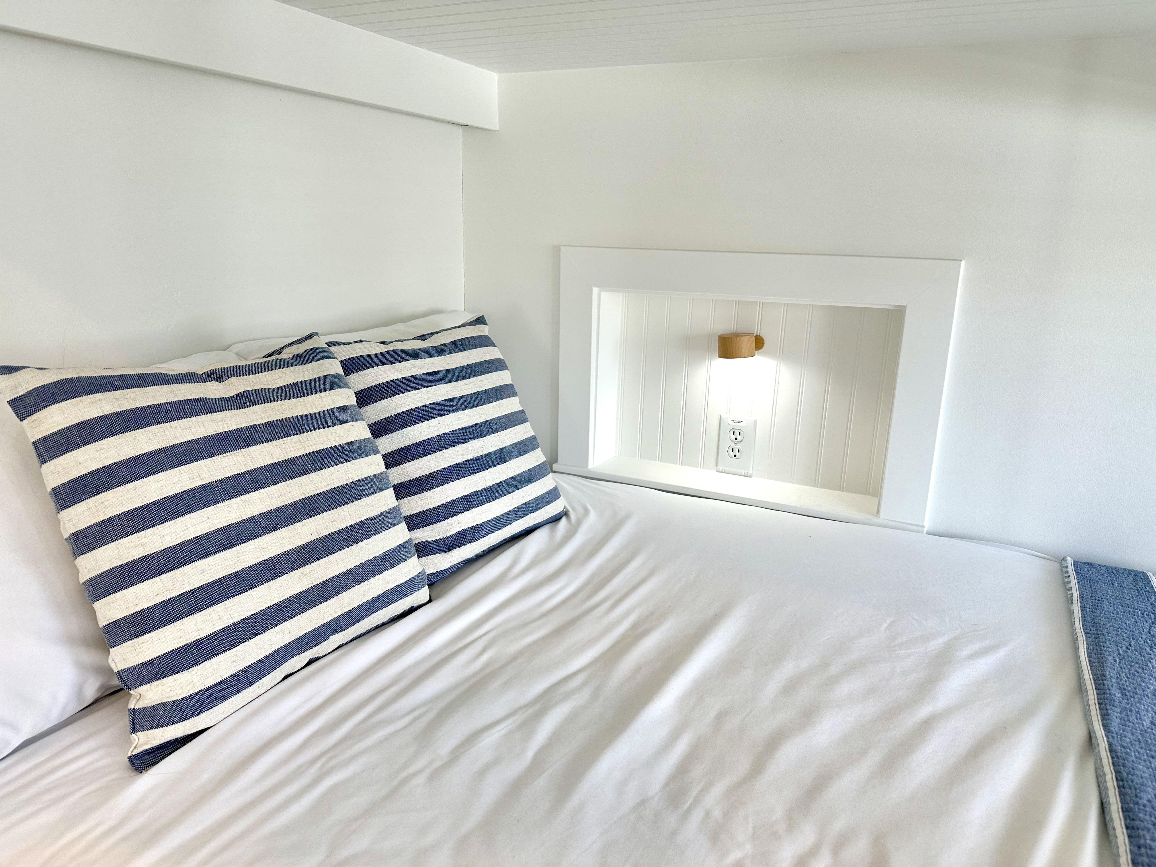 Built-in bunk bed with an integrated recessed niche featuring wood-finish wall paneling, a wall-mounted light fixture, and a power outlet