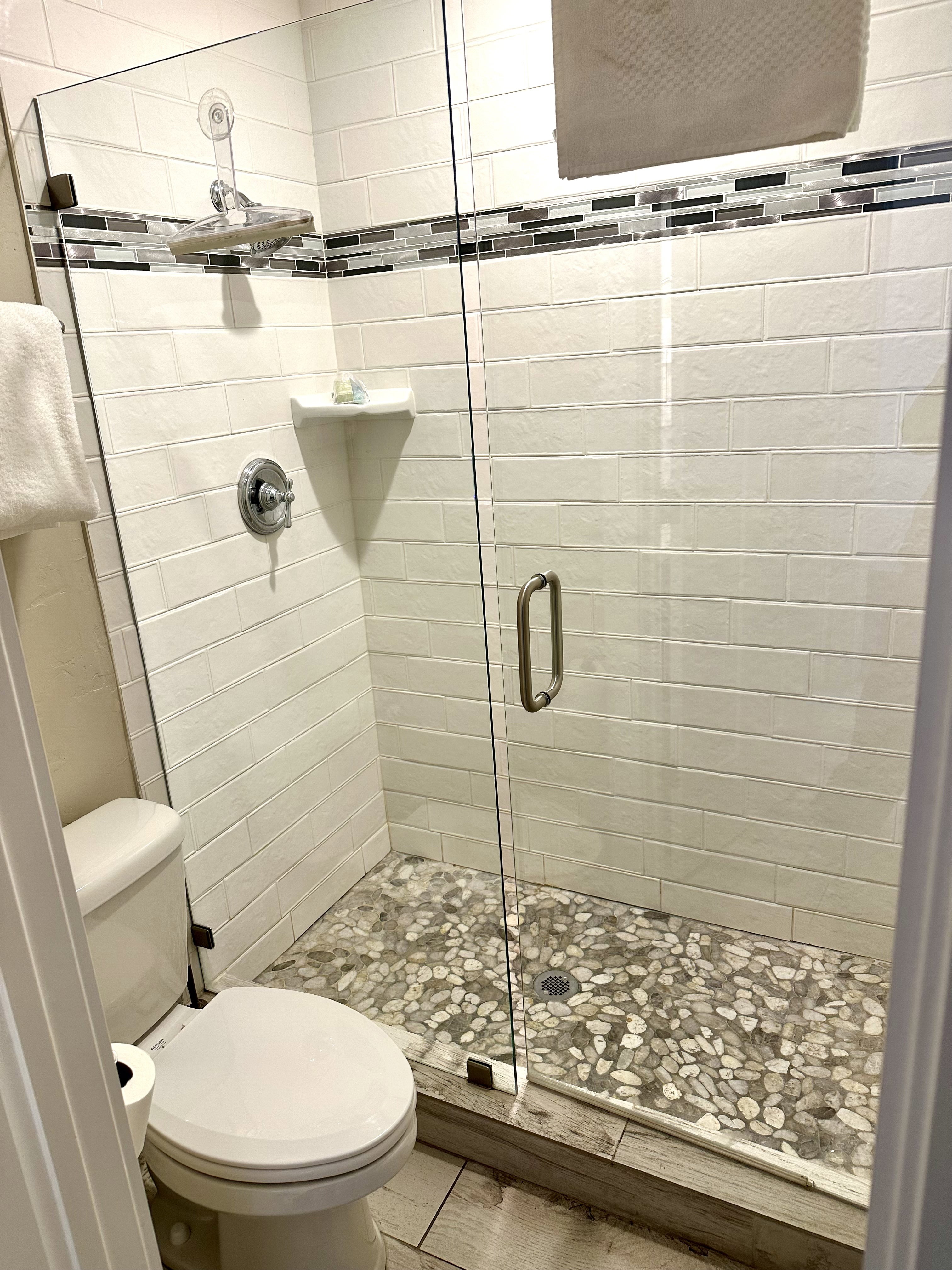 Walk-in shower with clear glass enclosure and pebble-tiled floor