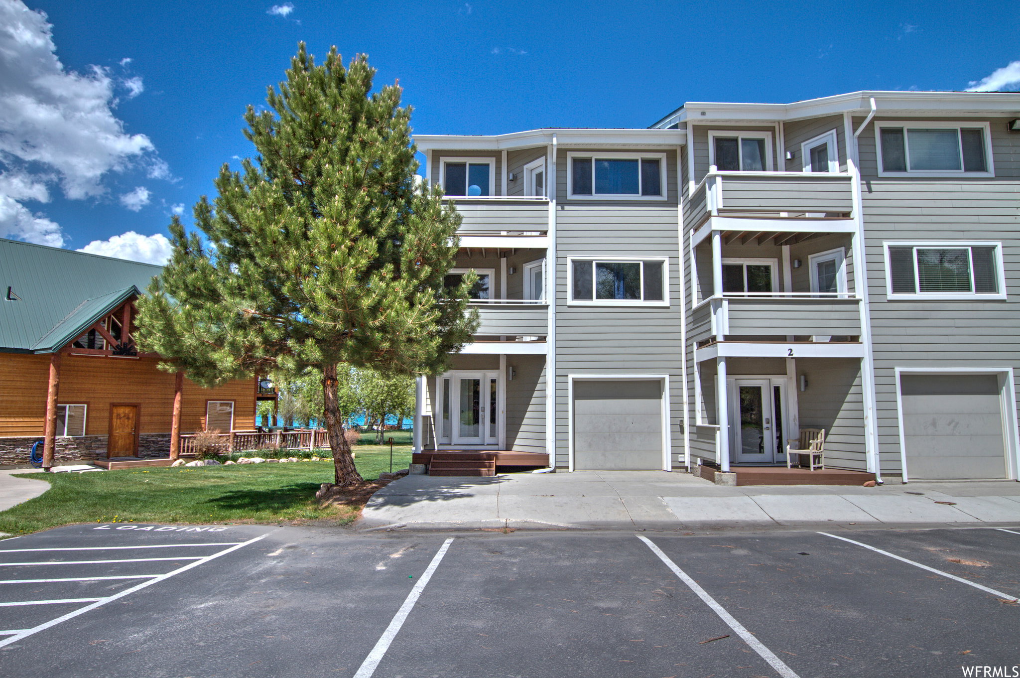 Multi-story building featuring light gray siding, white trim, and individual ground-level garages
