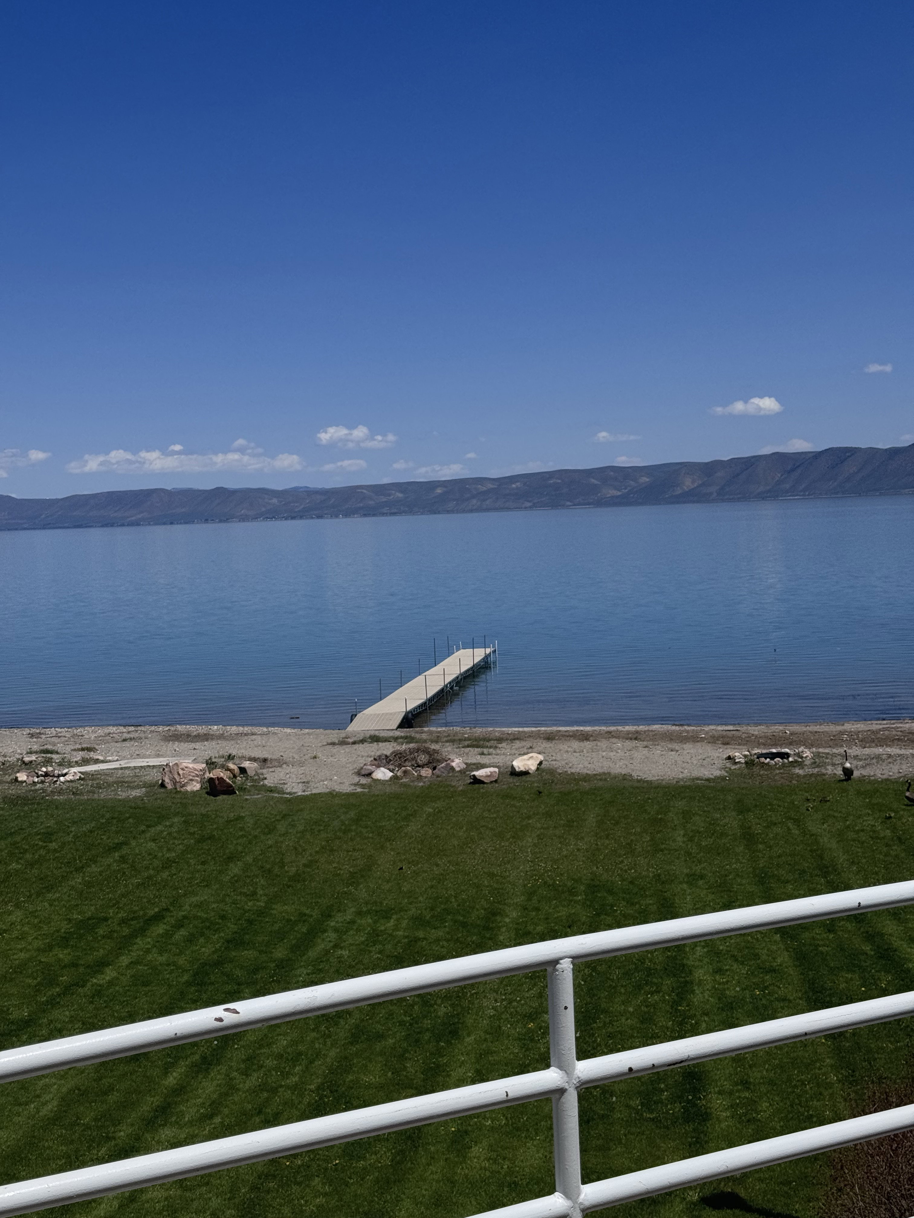 Expansive waterfront property featuring a private dock, a manicured lawn, a gravel beach, and distant mountain scenery