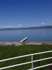 Expansive waterfront property featuring a private dock, a manicured lawn, a gravel beach, and distant mountain scenery