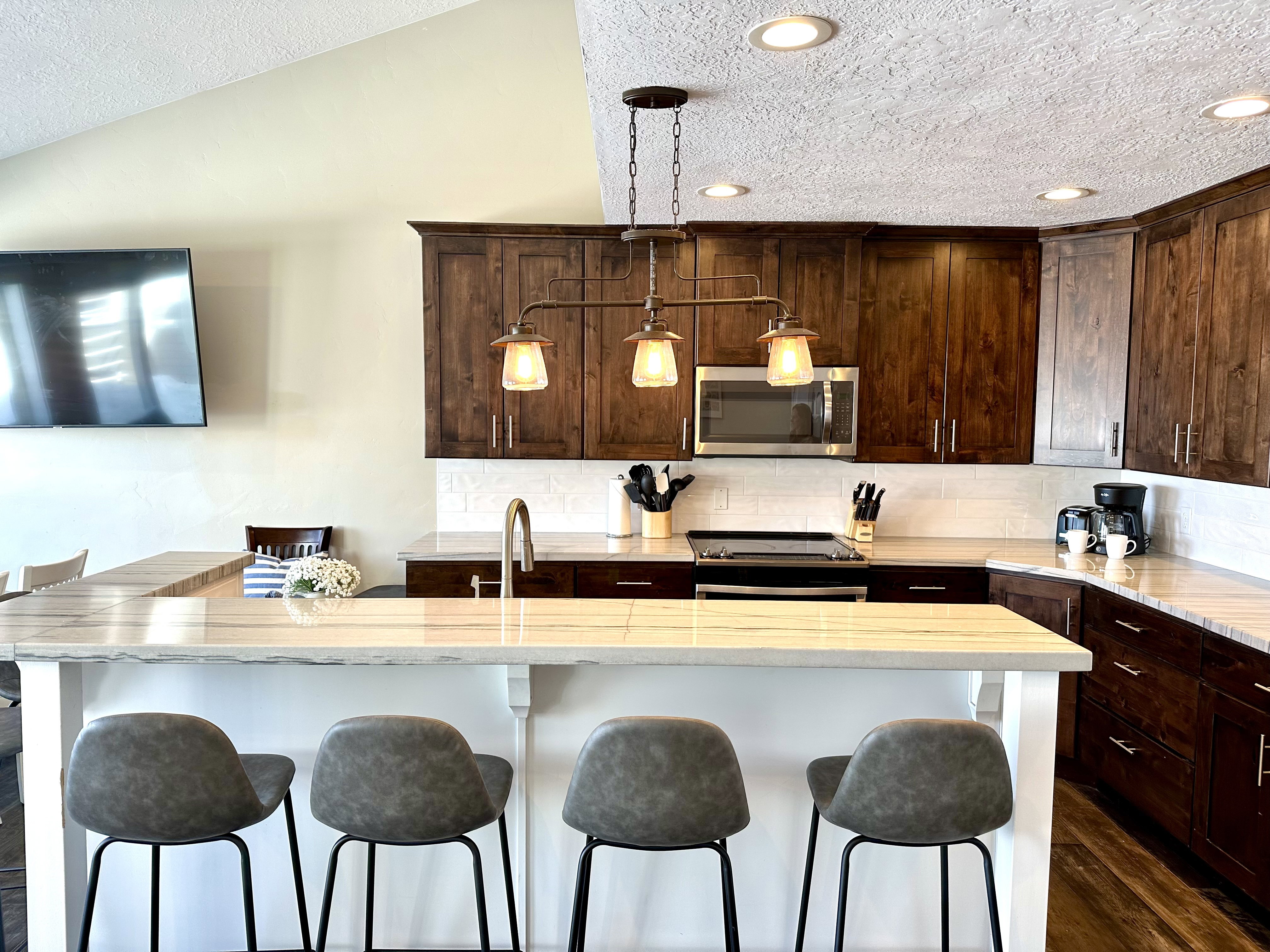 Kitchen featuring an expansive island with a light-toned countertop, dark wood cabinetry, white subway tile backsplash, stainless steel microwave, and recessed lighting