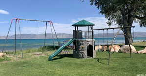 Expansive lawn area featuring a multi-component playset with a slide and climbing wall, two swing sets, and mature trees