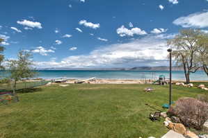 Expansive green lawn extending to a sandy shoreline with direct water access