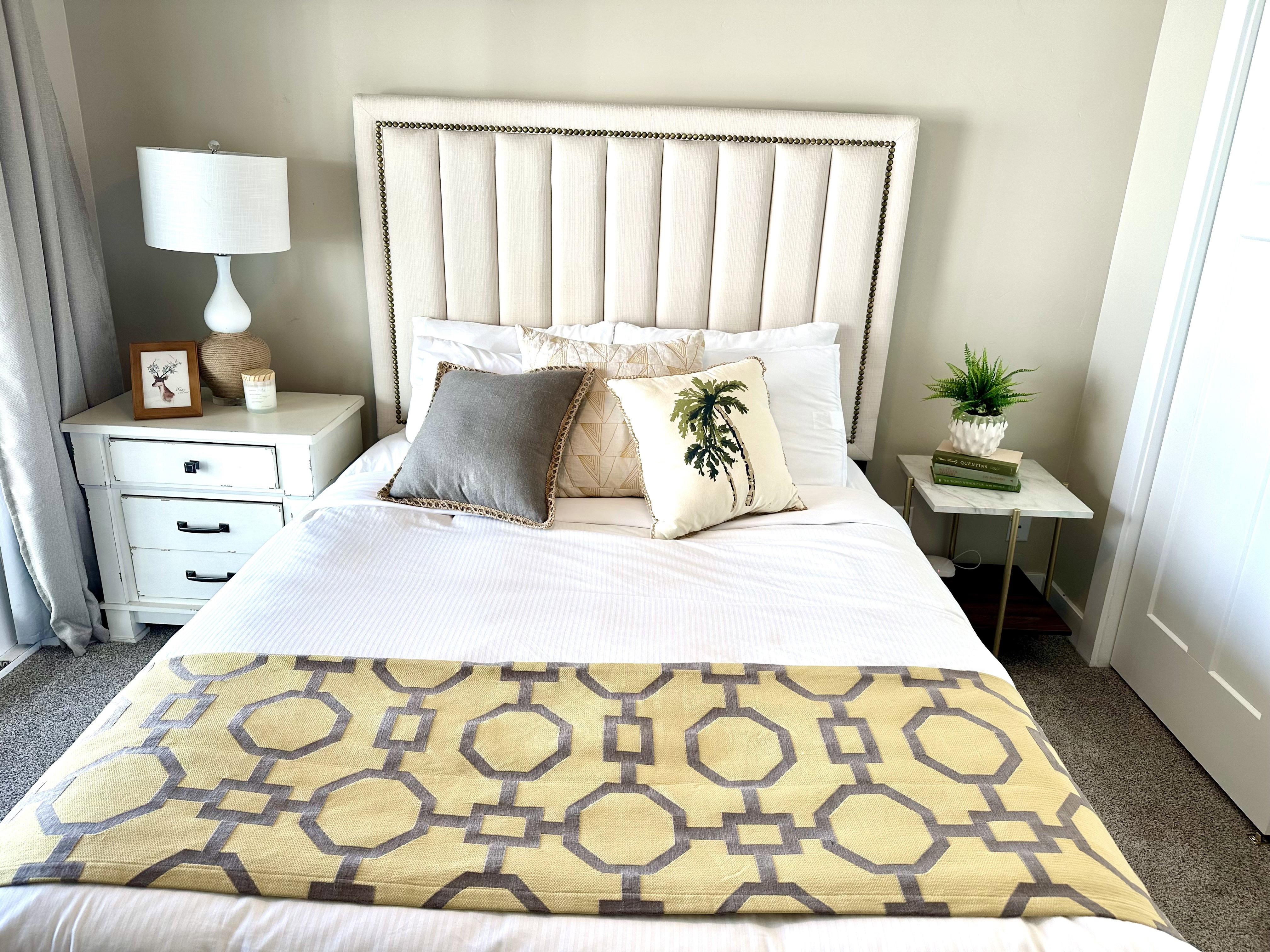 Upholstered channel-tufted headboard with nailhead trim, neutral wall color, and carpet flooring