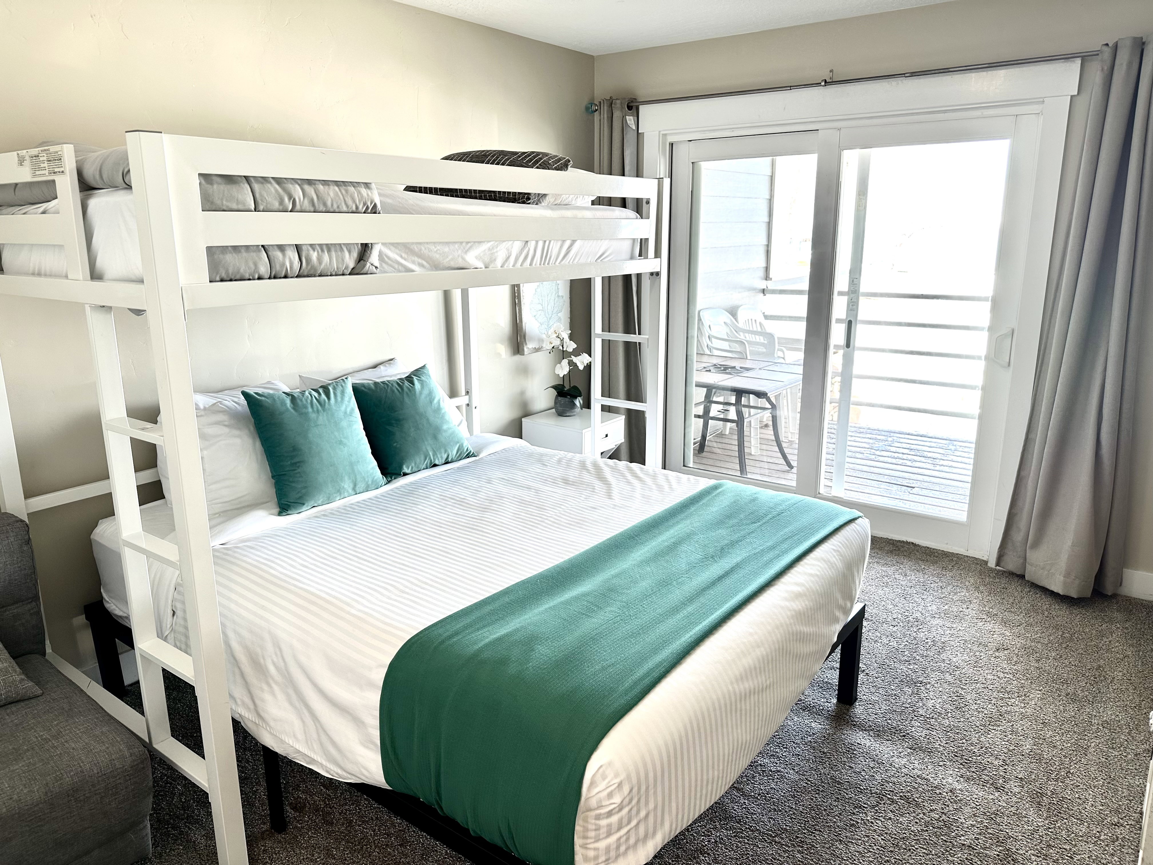 Room featuring a white metal bunk bed, neutral carpeting, and a white sliding glass door