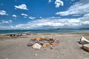 Lakeside property featuring a stone-lined fire pit, a private dock extending into the water, and expansive water frontage with mountain scenery