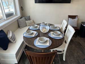 Built-in corner bench seating with window, dark wood-finish flooring, and light-toned wall paint