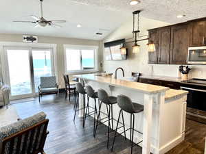 Open-concept common area featuring wood-finish flooring, a vaulted ceiling, and a kitchen island with seating