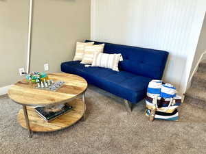 Carpeted room featuring a two-tier round wood-finish coffee table with metal legs and a white beadboard accent wall