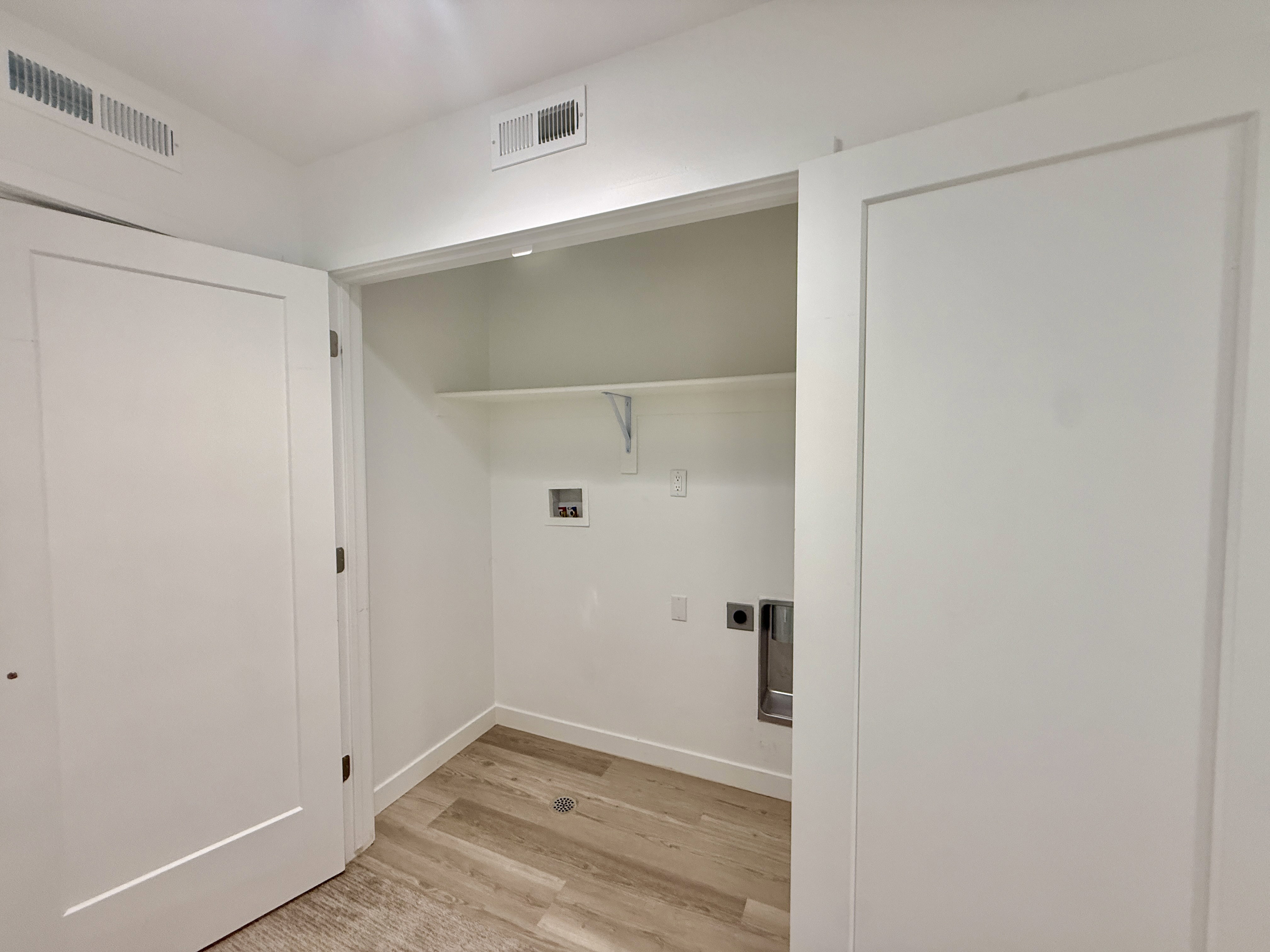 Dedicated laundry area featuring wood-finish flooring, white walls, and a built-in shelf