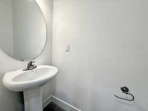 Pedestal sink with a polished chrome faucet, circular wall-mounted mirror, and dark wood-finish flooring