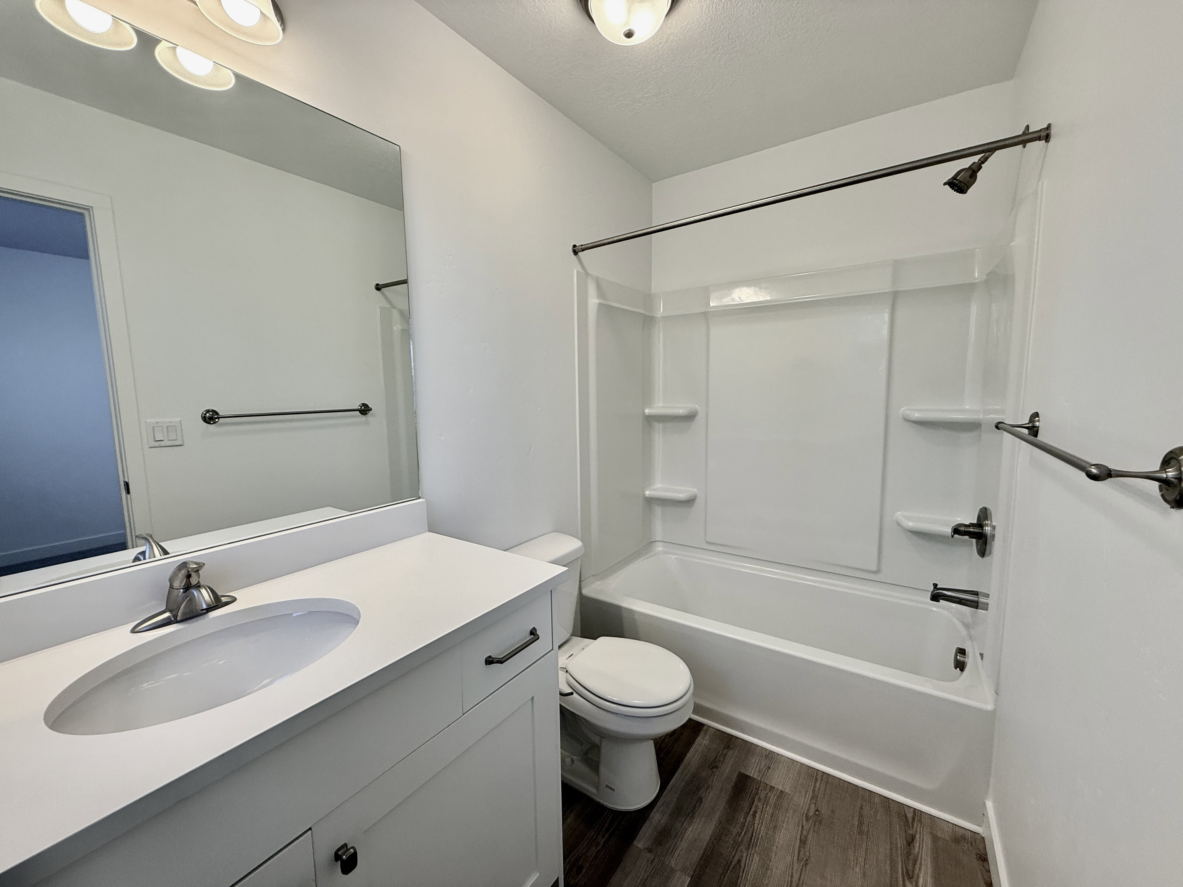 Bathroom featuring a white vanity with an integrated sink, a rectangular mirror, and a white tub/shower combination with built-in shelving
