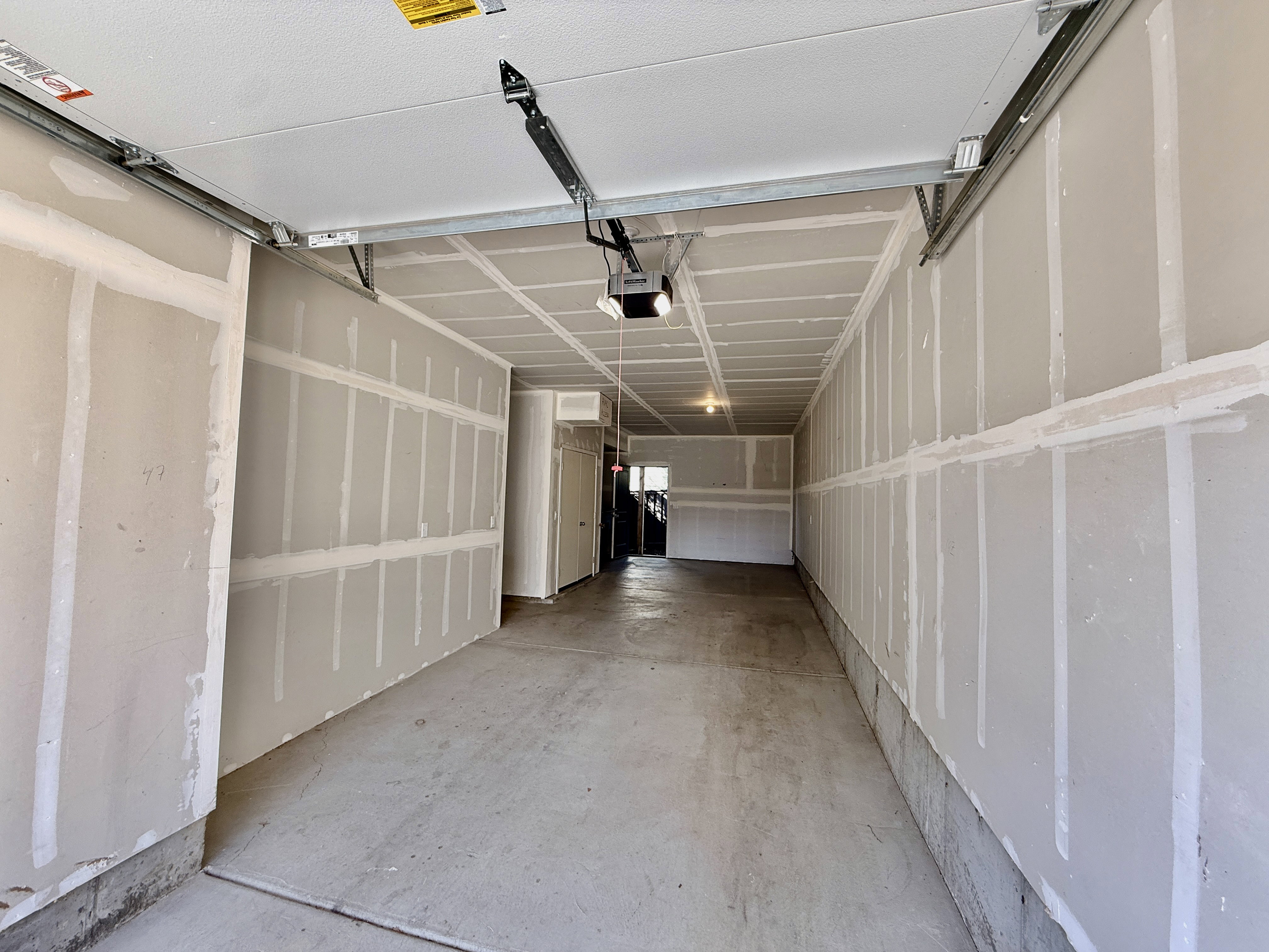 Garage interior featuring a concrete floor, unpainted drywall walls, and an overhead garage door opener