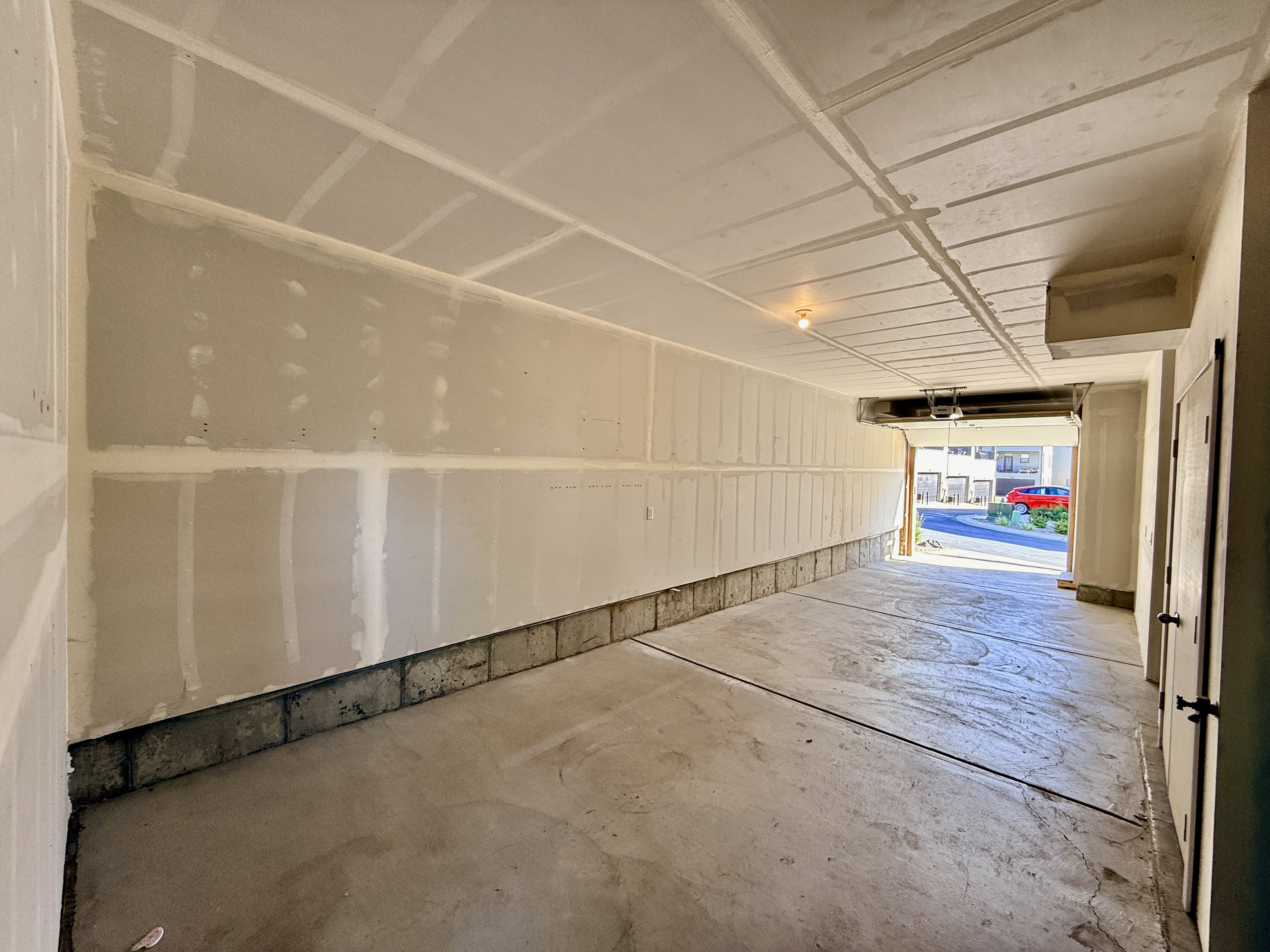 Spacious garage with unfinished drywall, concrete flooring, exposed ceiling joists, and an overhead garage door opener