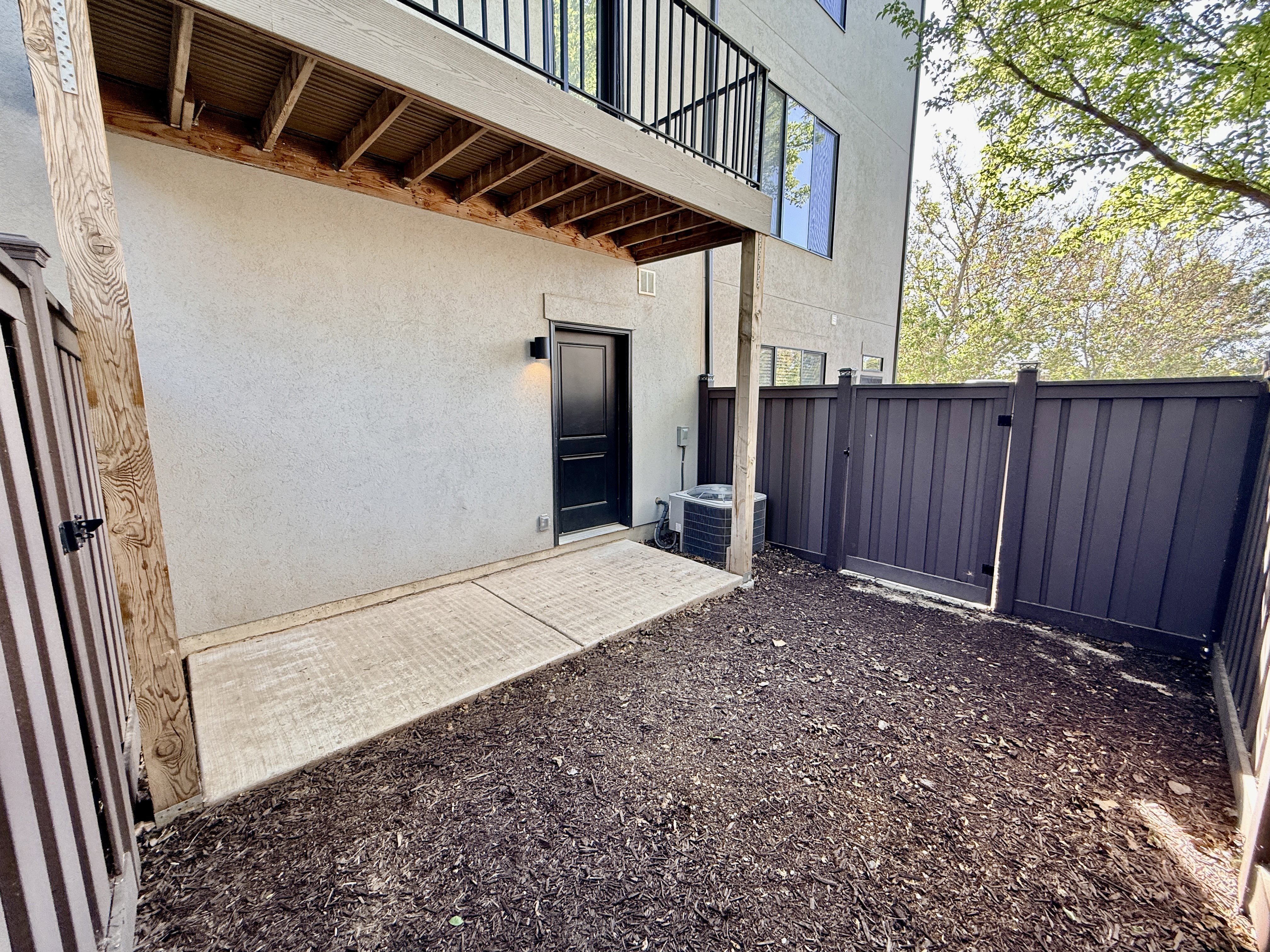 Private fenced patio space featuring a concrete pad and dark mulch ground cover
