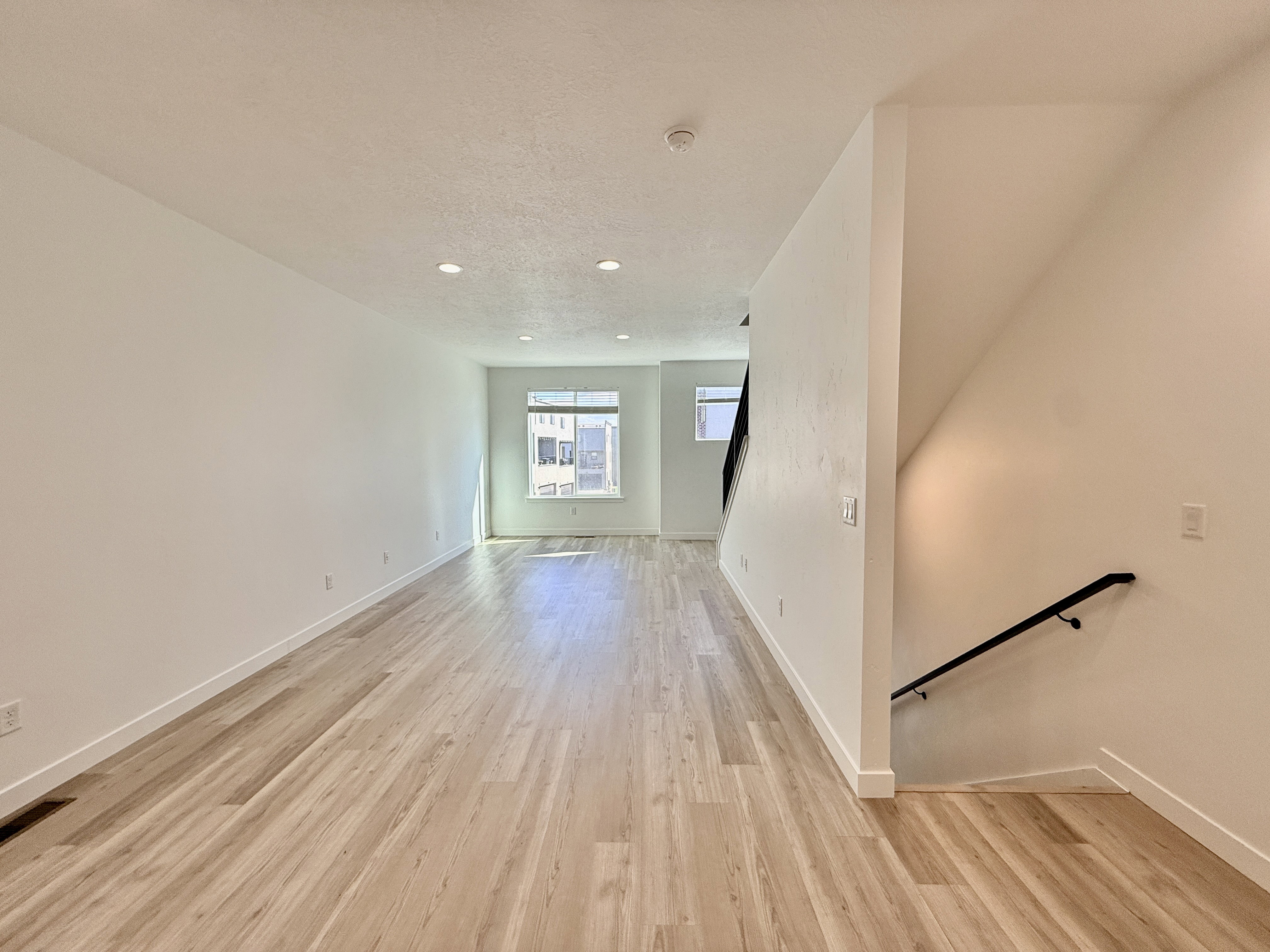 Open-concept living space featuring wood-finish flooring, recessed lighting, white walls, and a contemporary black handrail on the staircase