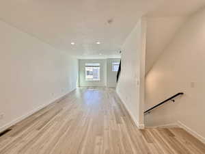 Open-concept living space featuring wood-finish flooring, recessed lighting, white walls, and a contemporary black handrail on the staircase