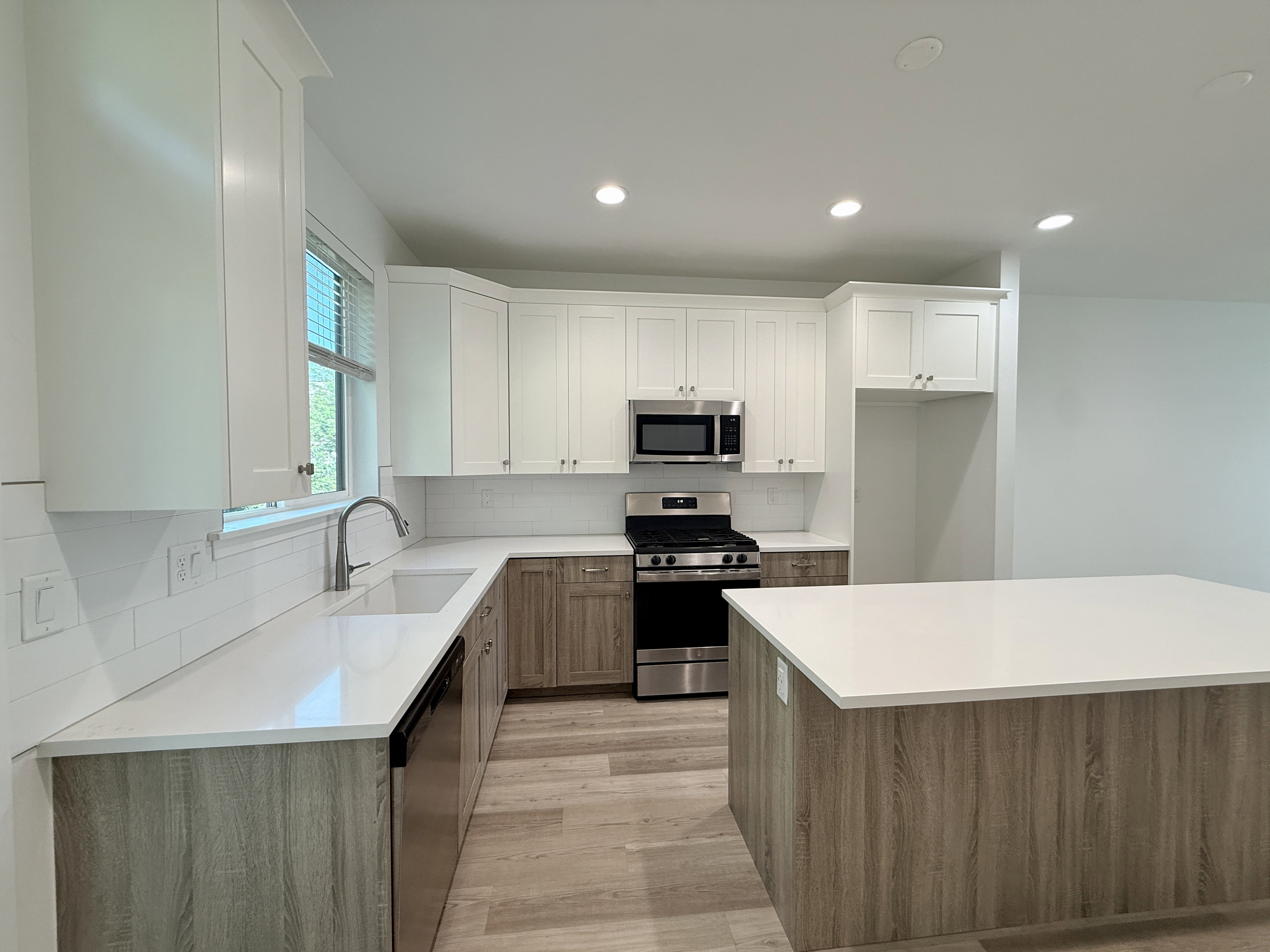 Modern kitchen featuring two-tone cabinetry, stainless steel appliances, white subway tile backsplash, recessed lighting, and a kitchen island with a light-toned countertop