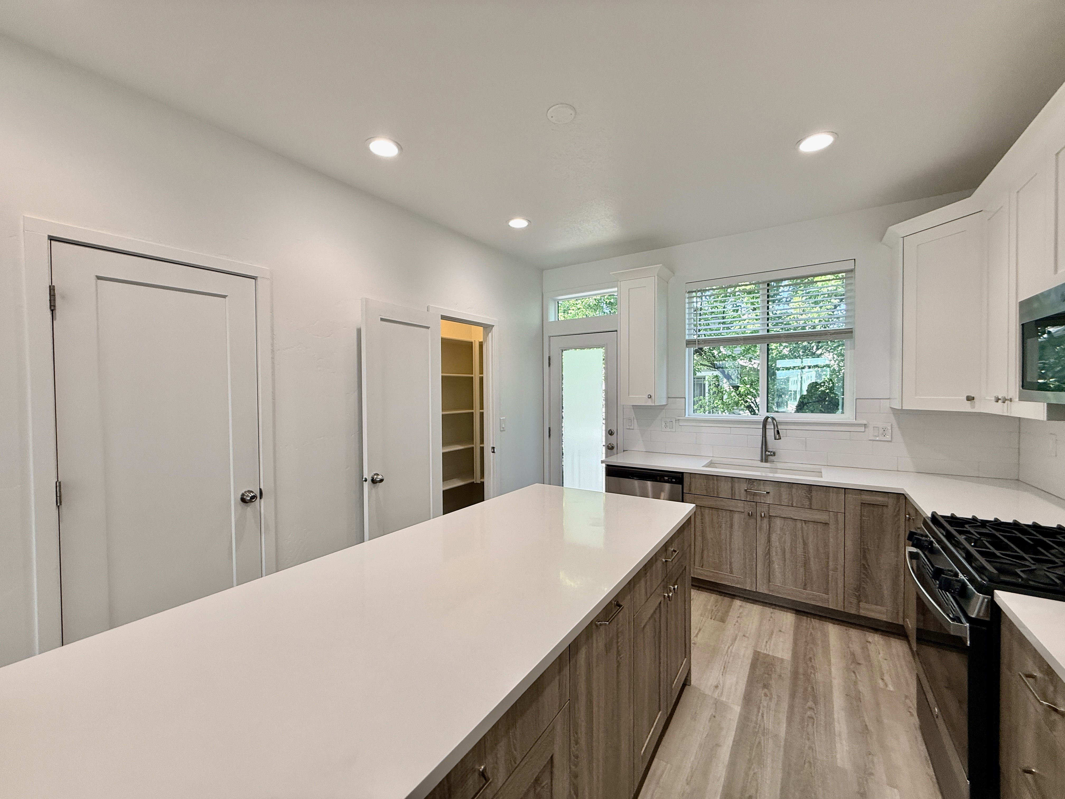 Modern kitchen featuring a large central island with a light-toned countertop, wood-finish flooring, white upper cabinetry, and wood-finish lower cabinetry