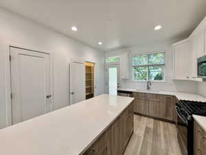 Modern kitchen featuring a large central island with a light-toned countertop, wood-finish flooring, white upper cabinetry, and wood-finish lower cabinetry