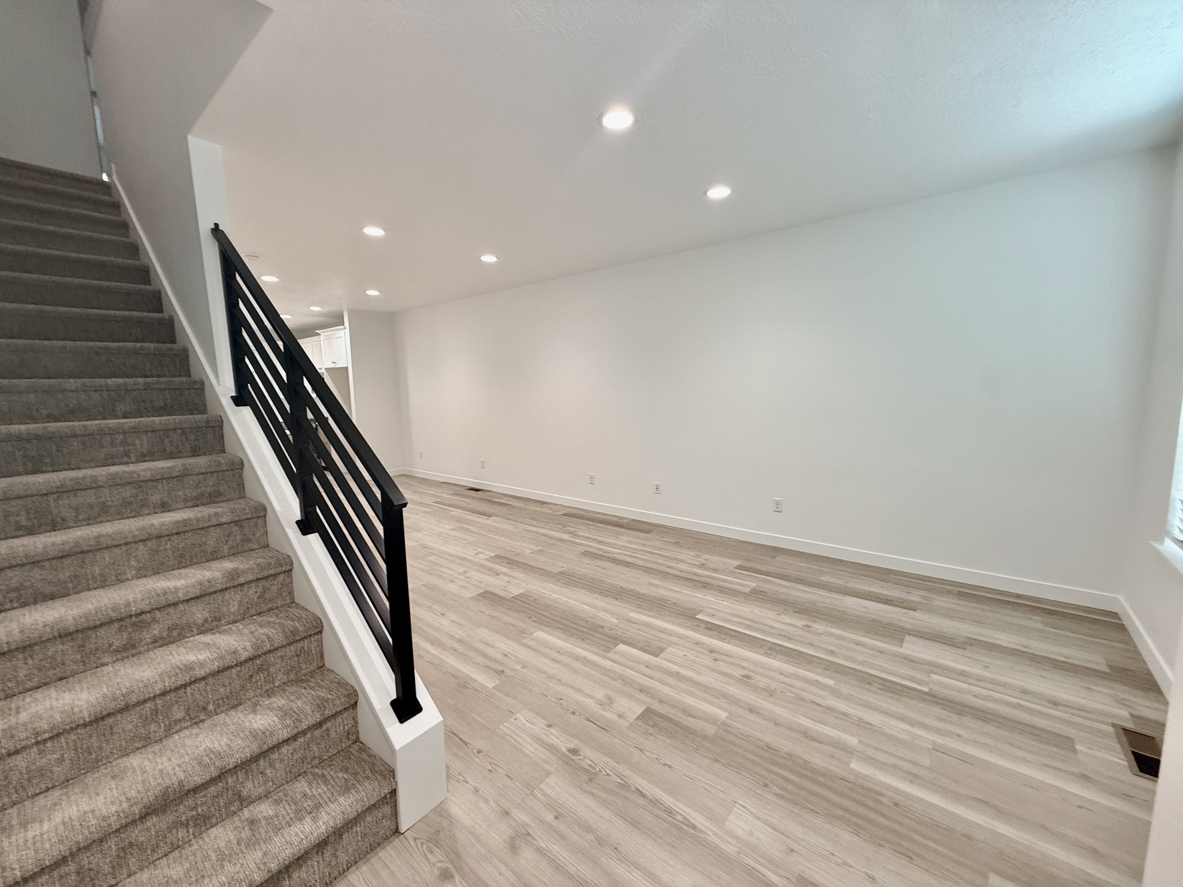 Open-concept living area featuring light wood-finish flooring, recessed ceiling lighting, and crisp white walls