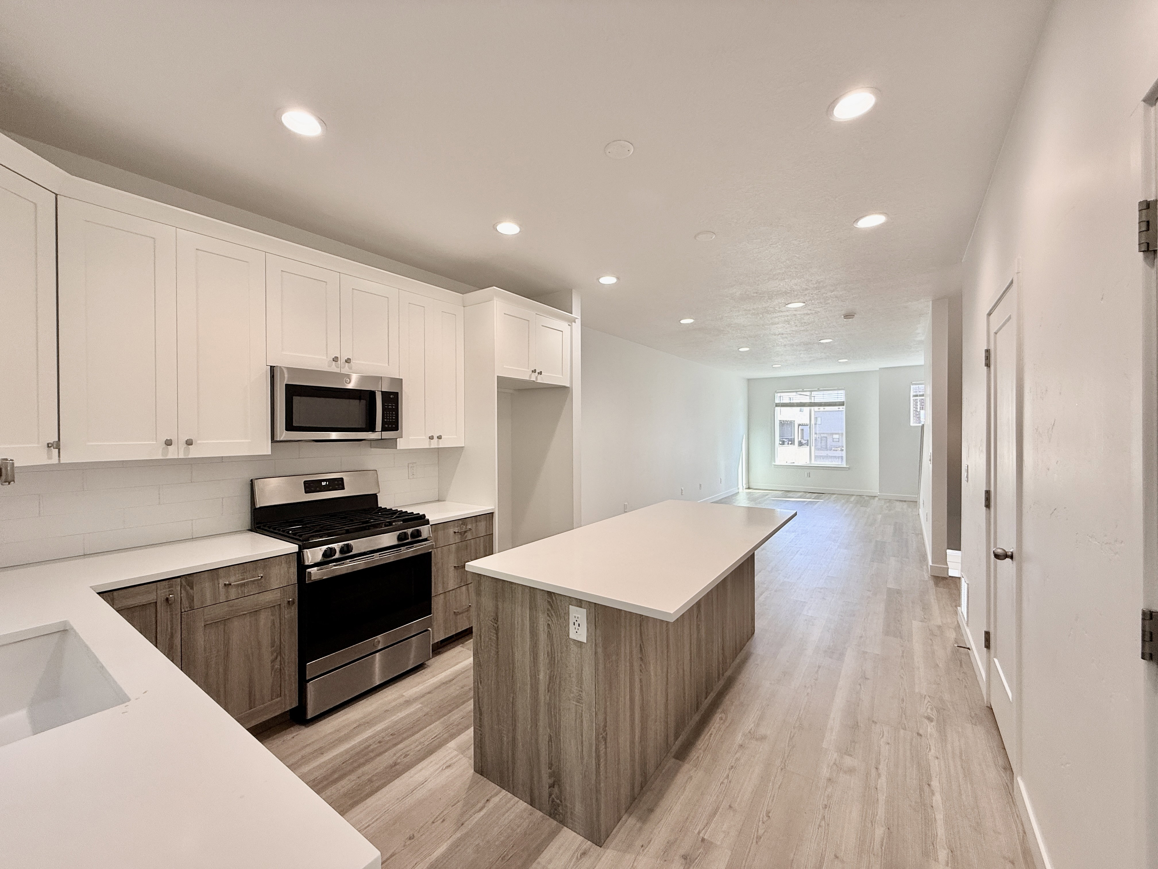 Modern kitchen featuring white shaker upper cabinetry and wood-finish lower cabinetry, stainless steel appliances, a subway tile backsplash, and light-toned countertops