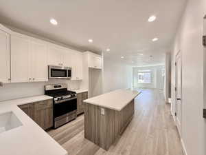 Modern kitchen featuring white shaker upper cabinetry and wood-finish lower cabinetry, stainless steel appliances, a subway tile backsplash, and light-toned countertops
