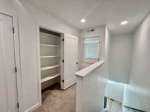Upper-level hallway featuring a built-in shelving unit, neutral wall paint, recessed lighting, and carpeted flooring