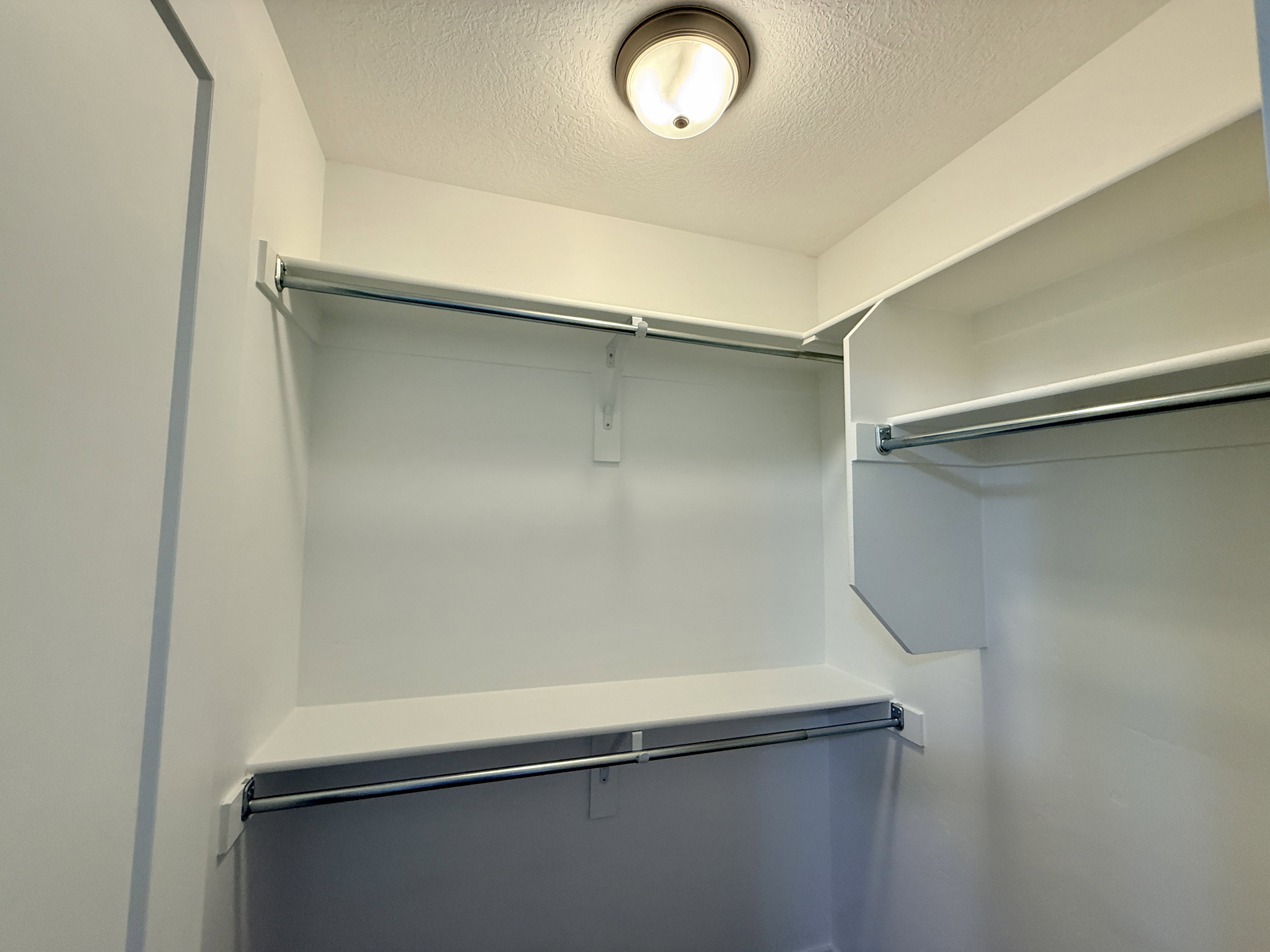 Walk-in closet featuring white shelving, multiple chrome hanging rods, and a ceiling-mounted flush light fixture