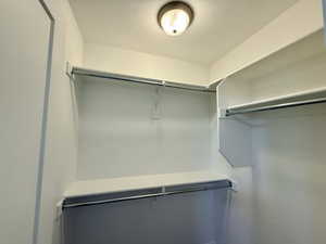 Walk-in closet featuring white shelving, multiple chrome hanging rods, and a ceiling-mounted flush light fixture
