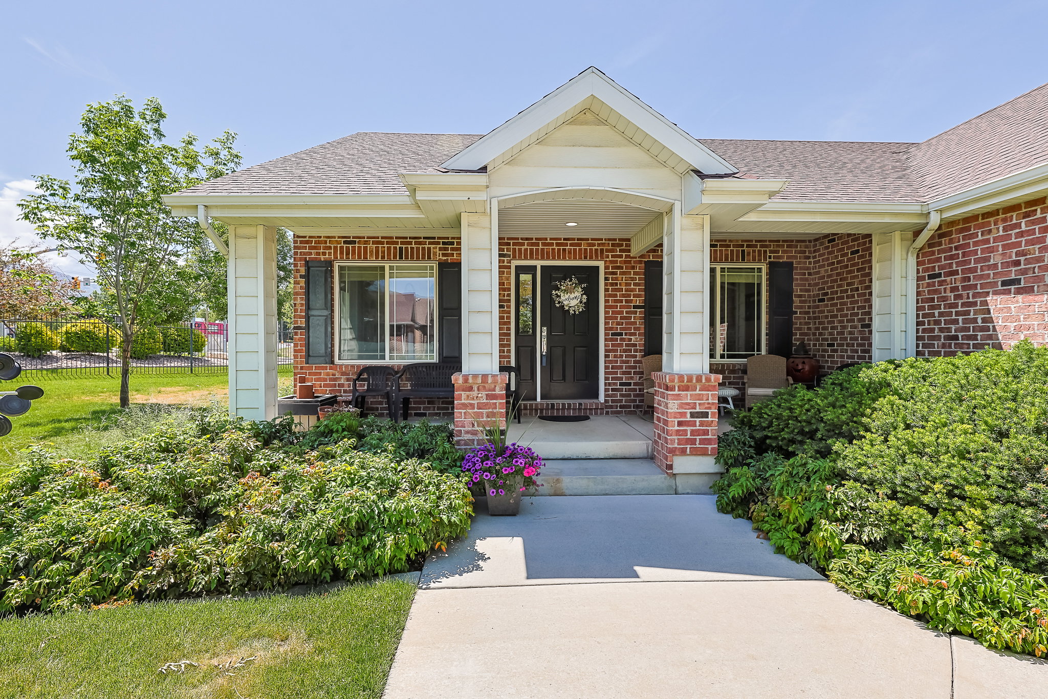 Brick facade home with a covered front porch, white columns, a dark entry door, and manicured shrubbery
