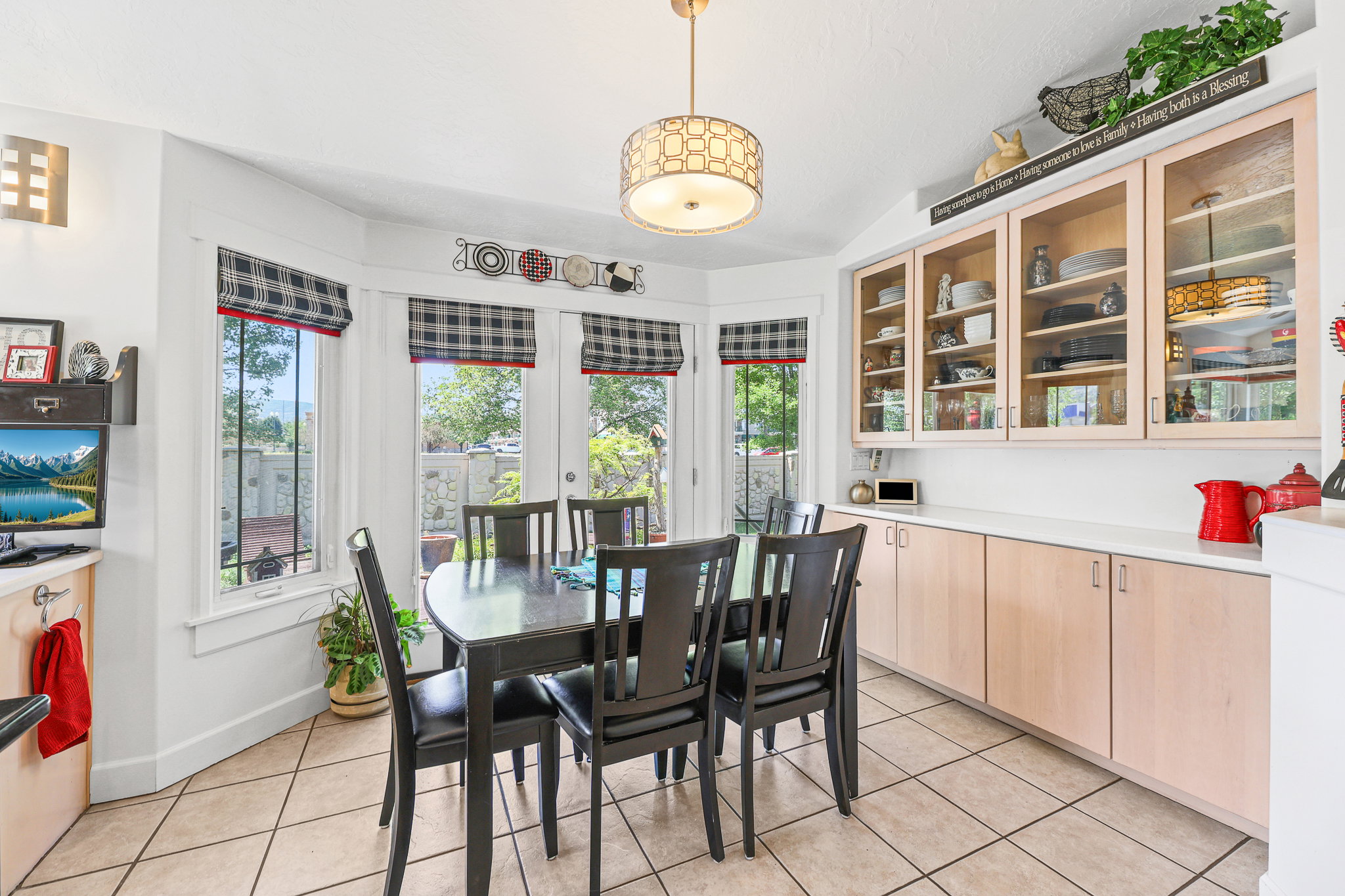 Dining area featuring a bay window with multiple panes, a neutral tile floor, a decorative ceiling light fixture, built-in lower cabinets with a light countertop, and upper cabinets with glass-front doors