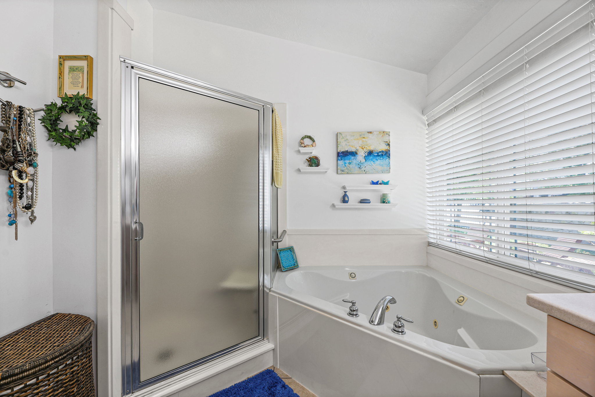 Bathroom featuring a shower enclosure with a frosted glass door, an integrated jetted tub with polished chrome fixtures, white window blinds, and white wall shelving