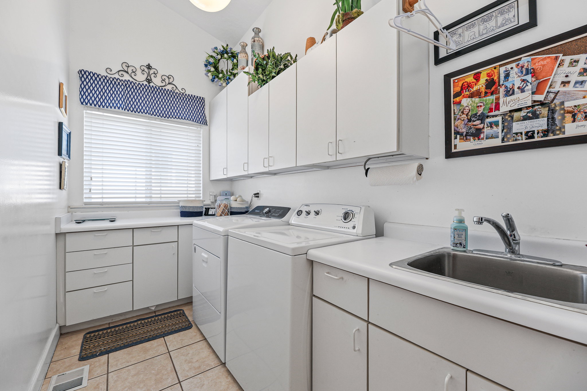 Bright utility room featuring ample white cabinetry, integrated sink, and a window with white blinds