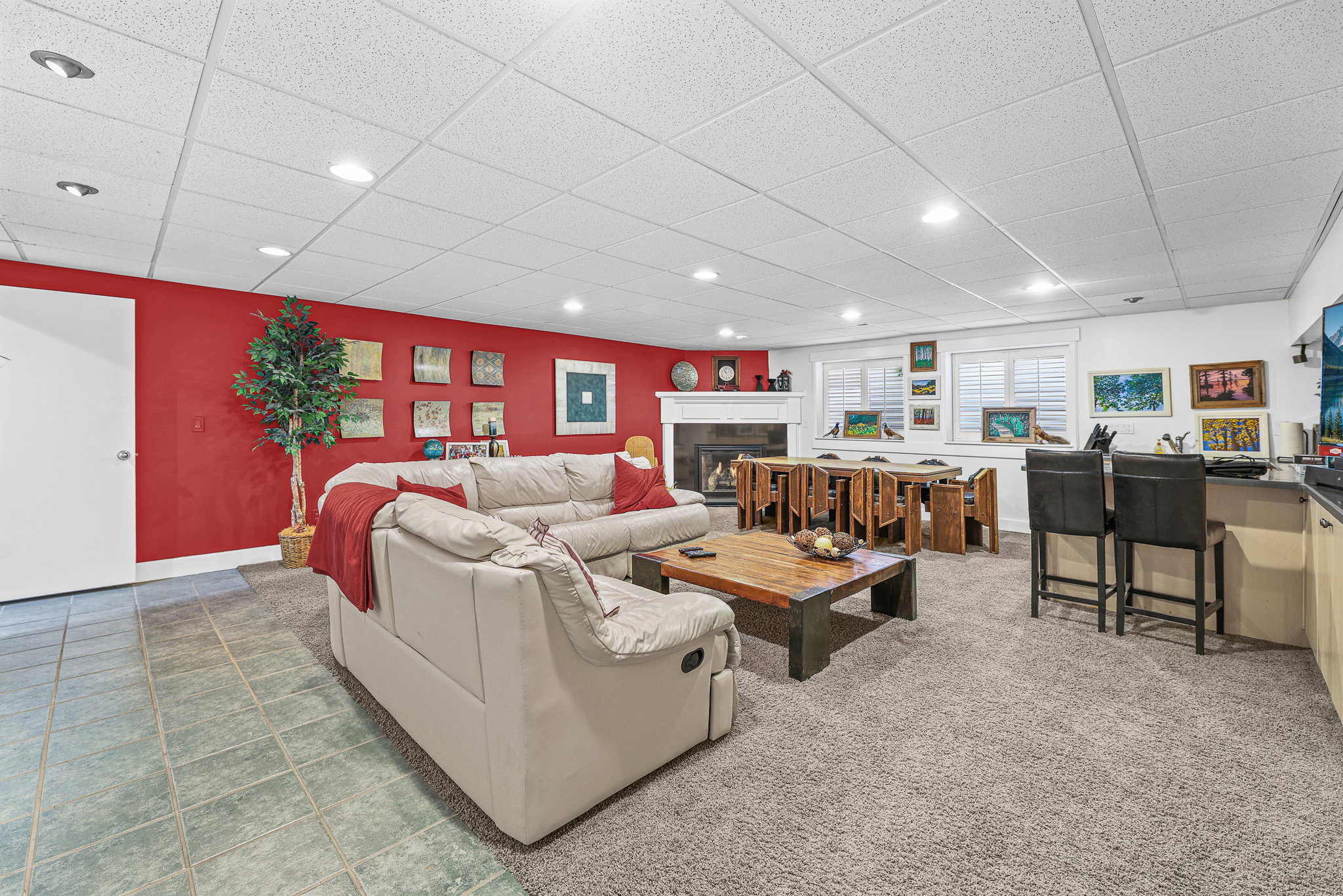 Open-concept living space with recessed lighting, a built-in wet bar, a fireplace with a white mantel, and multiple windows with white shutters