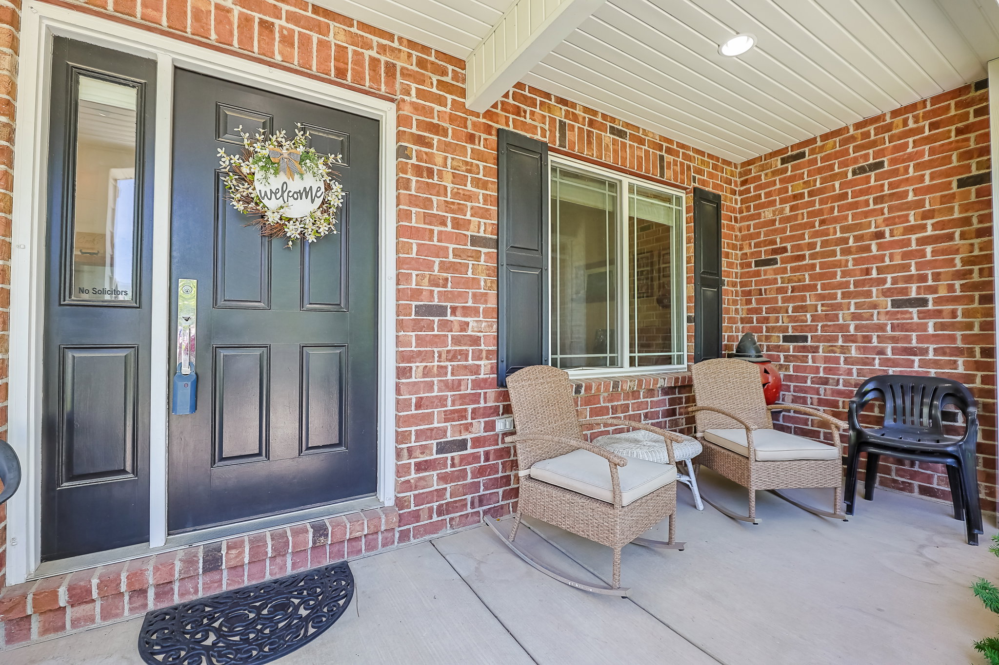 Brick exterior with a covered porch, featuring a paneled entry door with sidelight, and a window with dark shutters