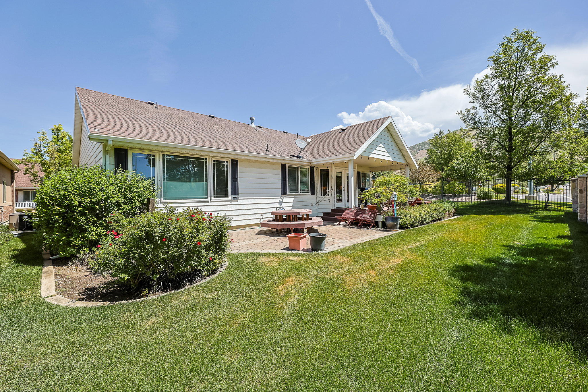 Expansive rear yard featuring a covered patio, a manicured lawn, established landscaping, and mature trees