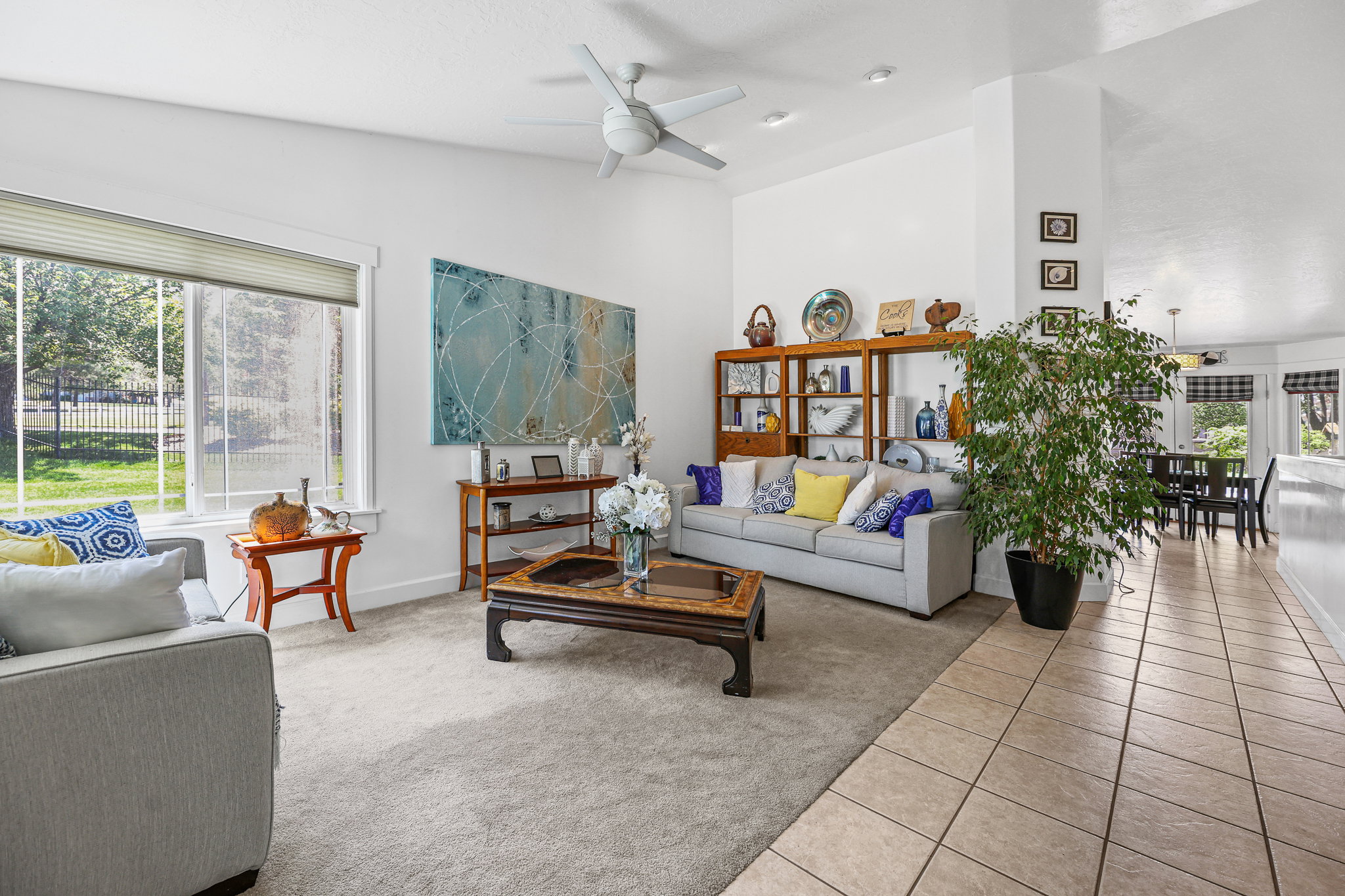 Bright living area featuring a large window, vaulted ceilings, a ceiling fan, and carpeted flooring