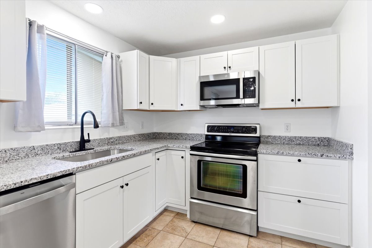 Kitchen featuring white shaker-style cabinetry, stainless steel appliances, speckled countertops, and a stainless steel sink with a matte black gooseneck faucet